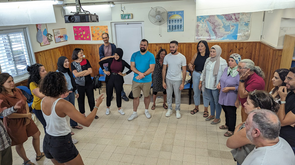 A group of Jewish and Arab teachers standing in a circle laughing