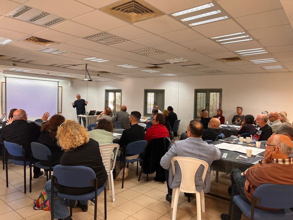 Teachers seated at tables looking at a slideshow being projected with their backs facing
