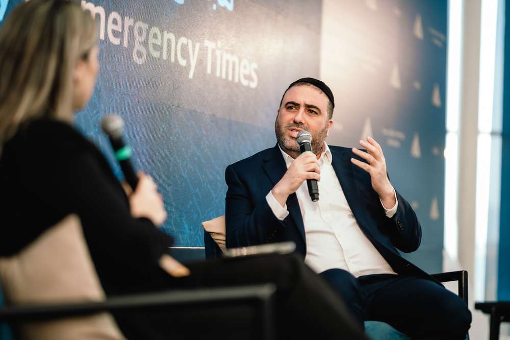 Moshe Arbel sitting with a microphoe inn nhis right hand looking left of center to the journalist interviewing him