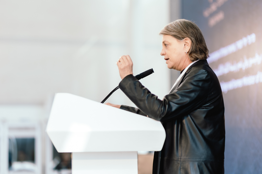 Yuli Tamir facing the left standing behind a podium with a mic