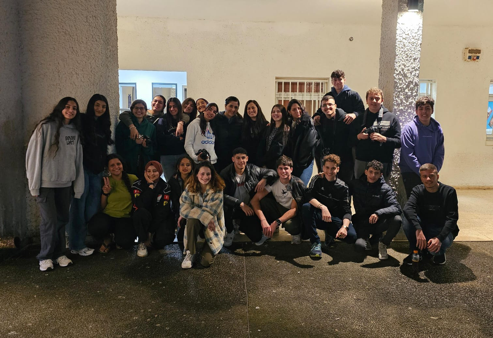 Through Others' Eyes students smiling at the camera, half are sitting and half are standing