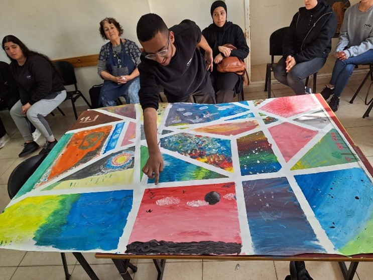 Students and staff sitting and one student standing up and pointing to a section of a painting