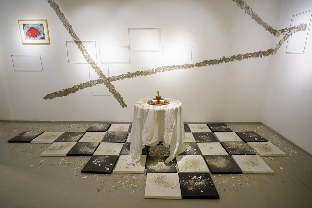 An exhibit featuring a table with a white tablecloth on a checkered floor against white walls with abstract lines