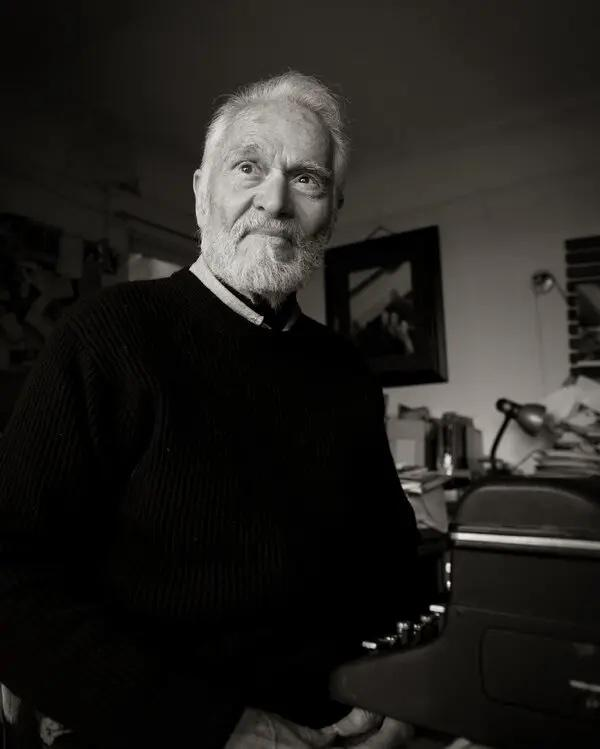 A black and white photo of Herb Gold in his later years, wearing a black sweater and up to the left, past the camera 