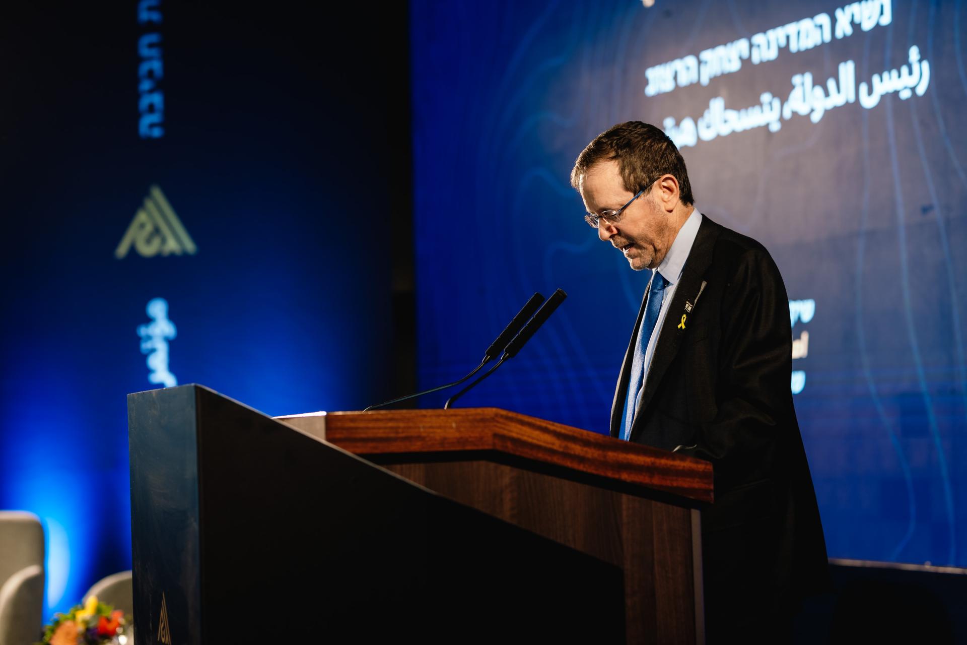 President Herzog behind a podium speaking into a microphone at the givat haviva annual conference